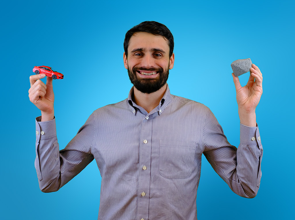 Ein MISAPOR Mitarbeiter mit Spielzeugauto in der einen und MISAPOR Schaumglasschotter in der anderen Hand